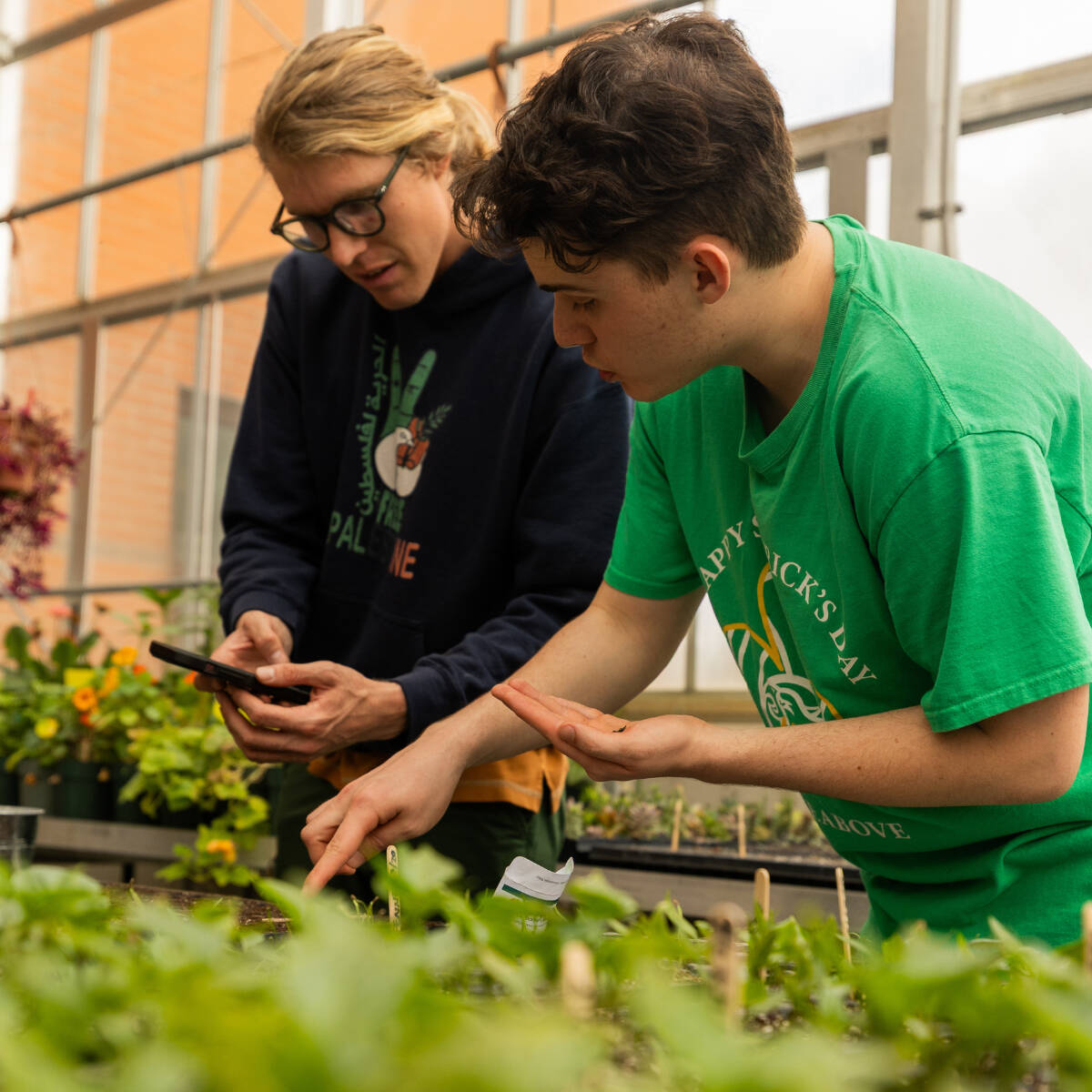 A student and a faculty member inspecting plants in the greenhouse